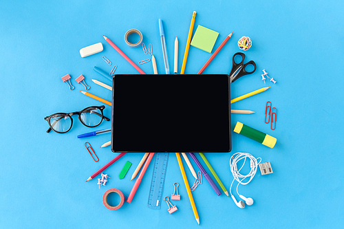 education, technology and object concept - tablet pc computer and stationery or school supplies on blue background