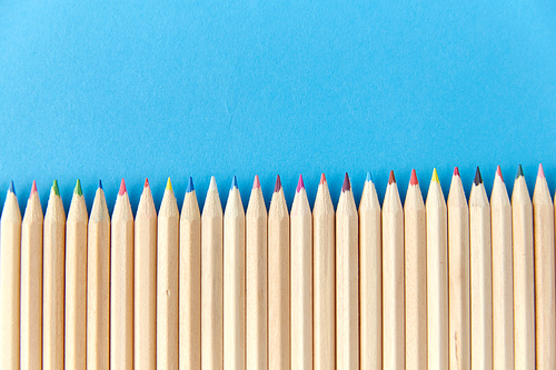 artistic tools, drawing, creativity and object concept - row of many coloring pencils on blue background