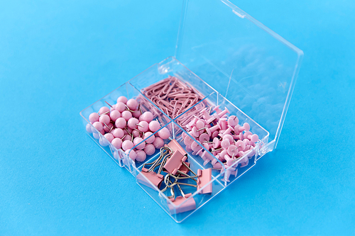 office supplies, stationery and object concept - pink pins and clips in plastic pox on blue background