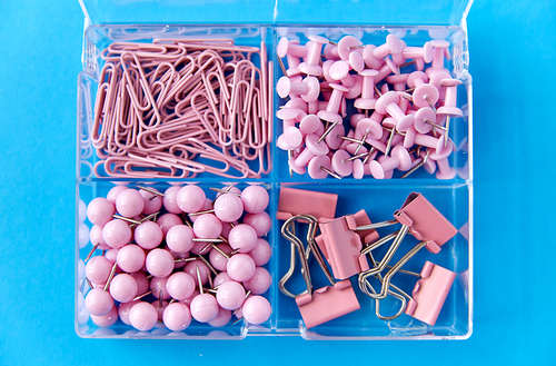 office supplies, stationery and object concept - pink pins and clips in plastic pox on blue background