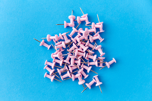 office supplies, stationery and object concept - heap of pink pins on blue background