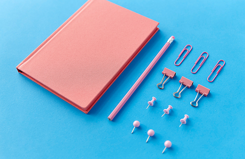 office supplies, stationery and object concept - pink notebook, pins, clips and pencil on blue background