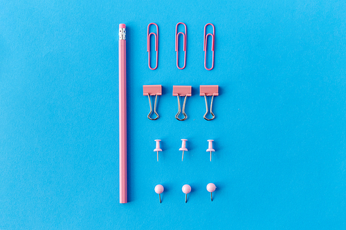 office supplies, stationery and object concept - pink pencil, pins and clips on blue background