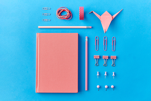 office supplies, stationery and object concept - pink notebook, pins, clips and pencils on blue background