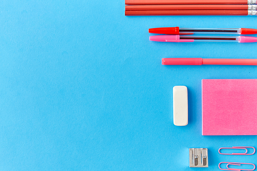 office supplies, stationery and object concept - pink sticky notes, clips, pens with pencils and eraser on blue background