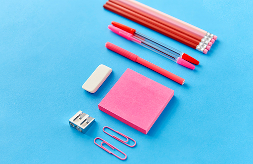 office supplies, stationery and object concept - pink sticky notes, clips, pens with pencils and eraser on blue background