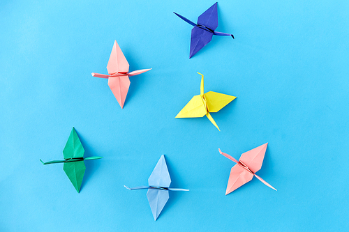 craft, hobby and creativity concept - multicolored origami paper cranes on blue background