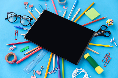 education, technology and object concept - tablet pc computer and stationery or school supplies on blue background