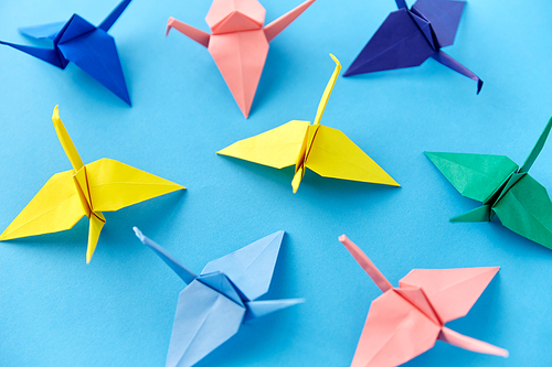 craft, hobby and creativity concept - close up of multicolored origami paper cranes on blue background