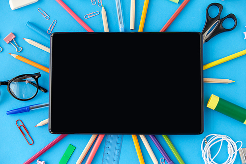 education, technology and object concept - tablet pc computer and stationery or school supplies on blue background