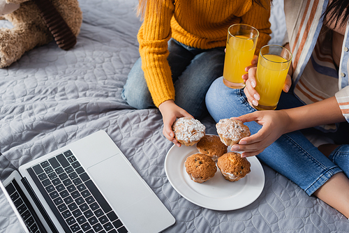 cropped view of mom and child holding orange juice and muffins while watching movie on laptop