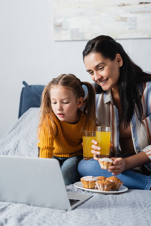 mother and daughter with muffins and orange juice watching film on laptop