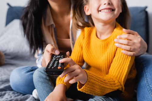 cropped view of happy child watching tv with mother on blurred background