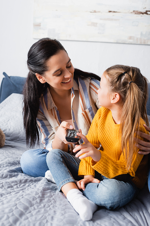 happy woman embracing daughter while holding tv remote controller
