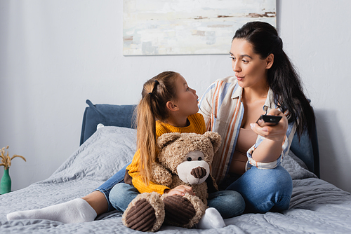 excited mother and daughter looking at each other while watching tv in bedroom