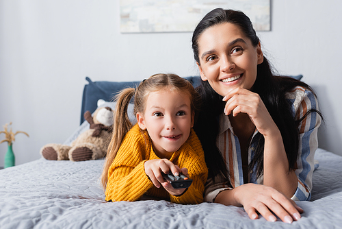 excited child clicking channels on remote controller while watching tv with mother