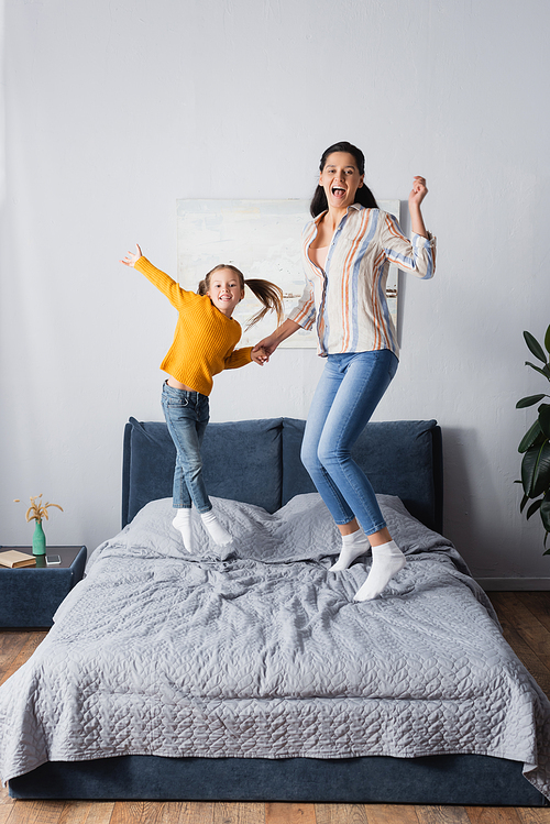 excited mother and daughter jumping on bed while 