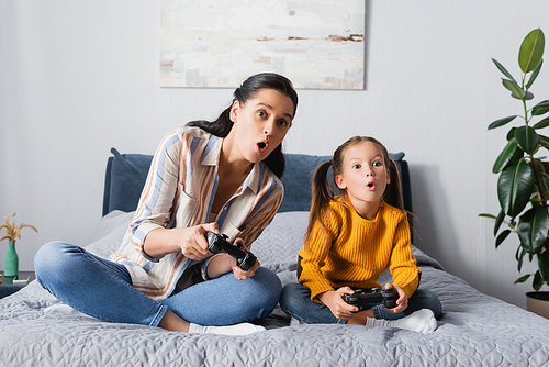 KYIV, UKRAINE - SEPTEMBER 15, 2020: shocked woman with daughter sitting with crossed legs and playing video game