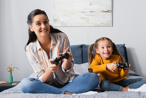 KYIV, UKRAINE - SEPTEMBER 15, 2020: happy girl with mother gaming with joysticks in bedroom