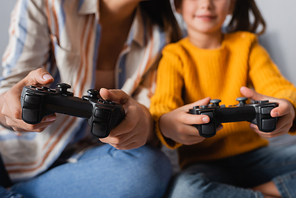 KYIV, UKRAINE - SEPTEMBER 15, 2020: cropped view of mother and daughter gaming with joysticks on blurred background, banner