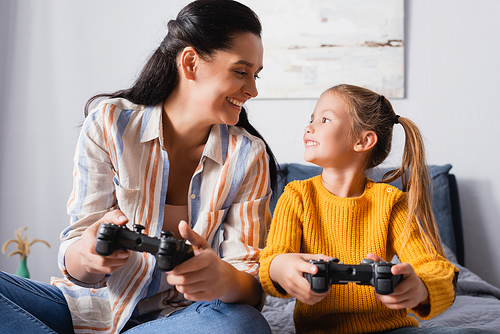 KYIV, UKRAINE - SEPTEMBER 15, 2020: happy mother and daughter looking at each other while playing video game