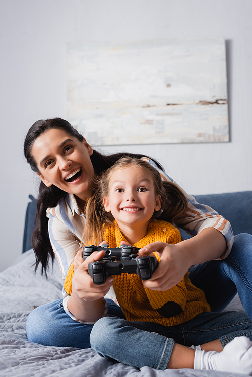 KYIV, UKRAINE - SEPTEMBER 15, 2020: excited mother and daughter playing video game in bedroom