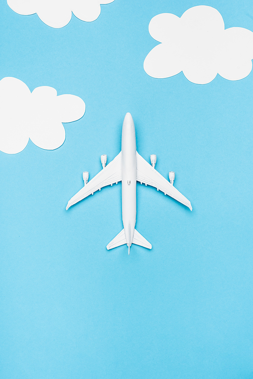top view of white plane model on blue background with white clouds