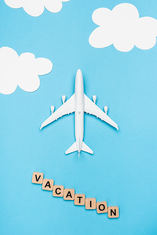 top view of plane model and cubes with word vacation on blue sky background