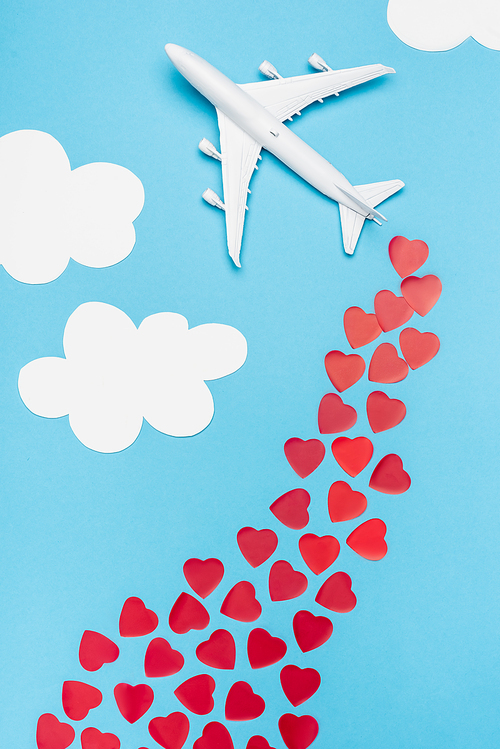 top view of plane model and red hearts on blue background with white clouds