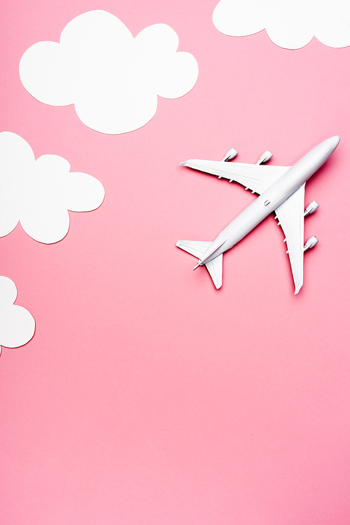 top view of white plane model on pink background with clouds