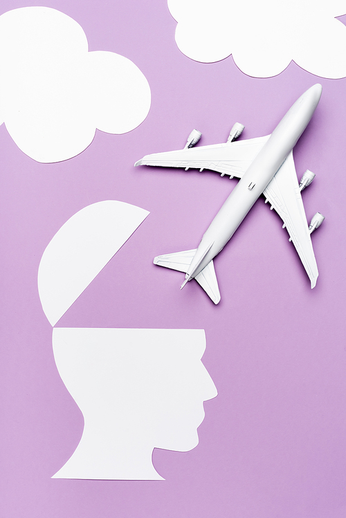 top view of white plane model and paper cut human head on violet background