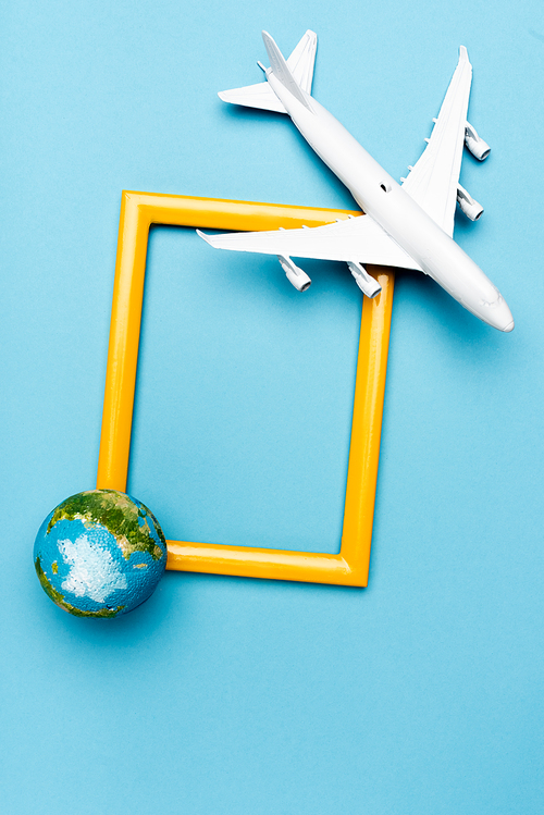 top view of white plane model, globe and empty frame on blue background