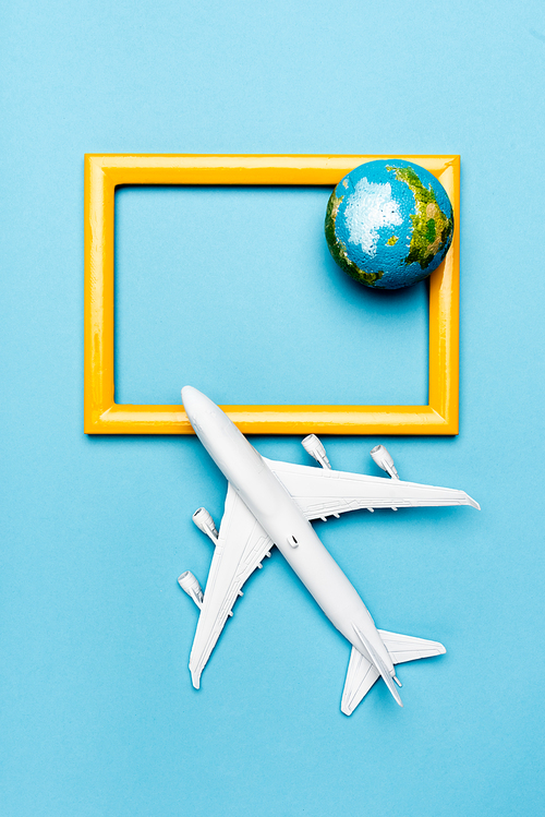 top view of white plane model, globe and empty frame on blue background
