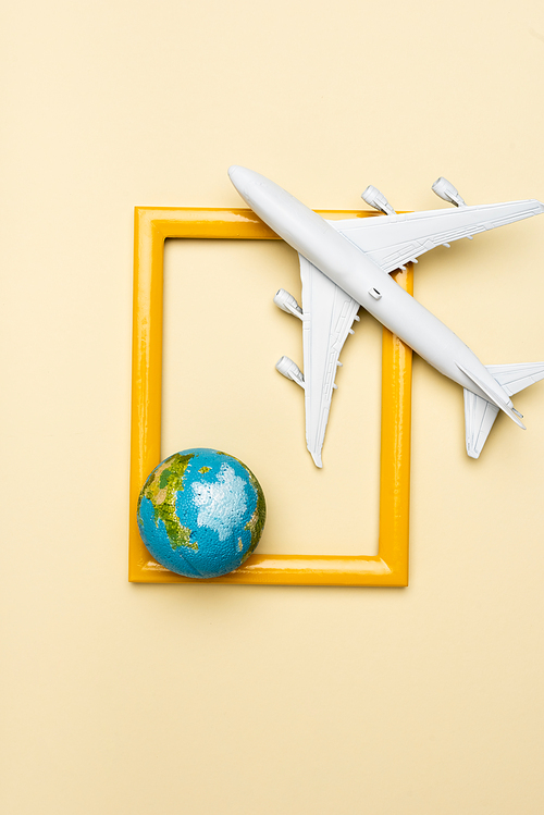 top view of white plane model, globe and empty frame on yellow background