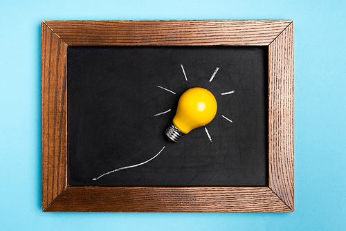 top view yellow light bulb and chalkboard on blue background