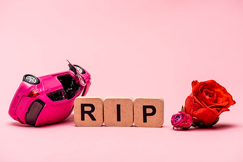 crashed car and word rip with flowers on pink background