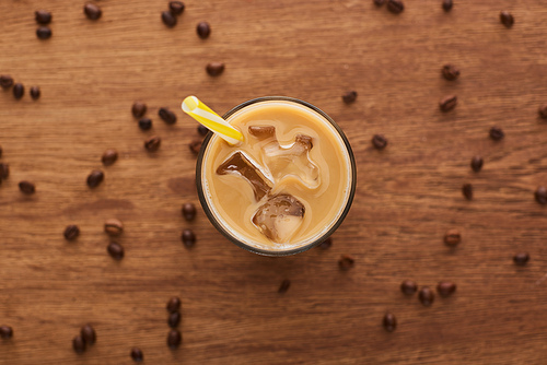 selective focus of ice coffee with straw in glass and coffee grains on wooden table