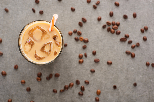 selective focus of ice coffee in glass with straw and coffee grains on grey background