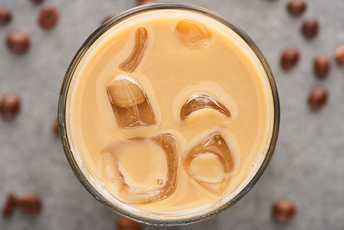 close up view of ice coffee in glass with straw and coffee grains on grey background