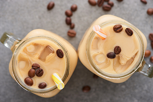 top view of tasty ice coffee with straws and coffee beans on grey background