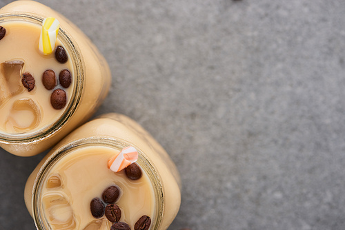 close up view of ice coffee in glass jars with straws near coffee grains on grey background with copy space