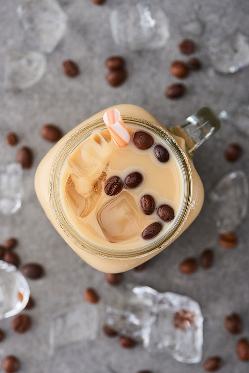 selective focus of ice coffee in glass jar with straw near coffee grains and ice cubes on grey background