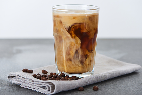 ice coffee mixing with milk in glass on napkin with coffee grains isolated on white