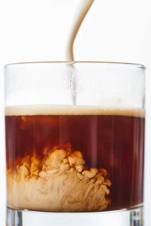 close up view of mil poring to coffee in glass isolated on white