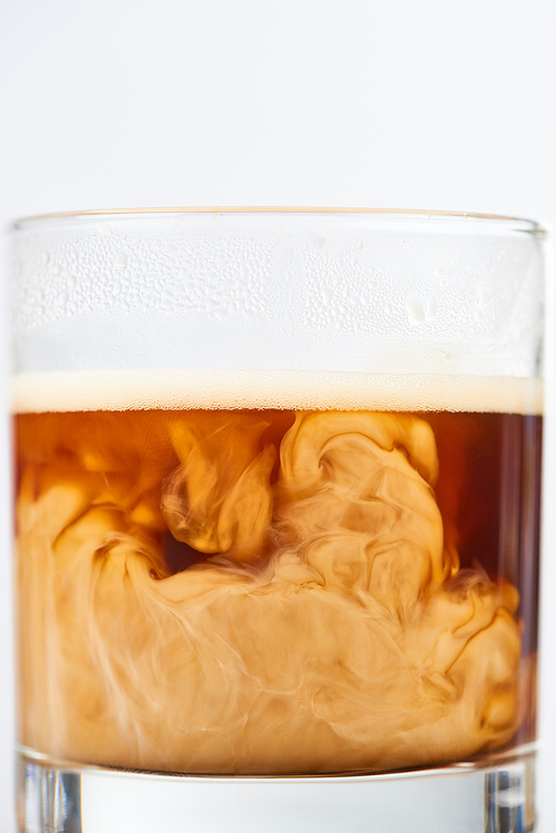 close up view of coffee mixing with milk in glass isolated on white