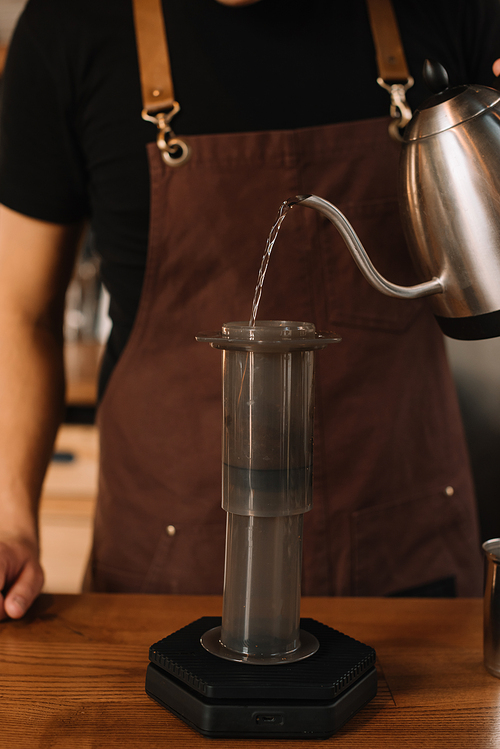 cropped view of barista pouring water from kettle in aeropress while preparing coffee