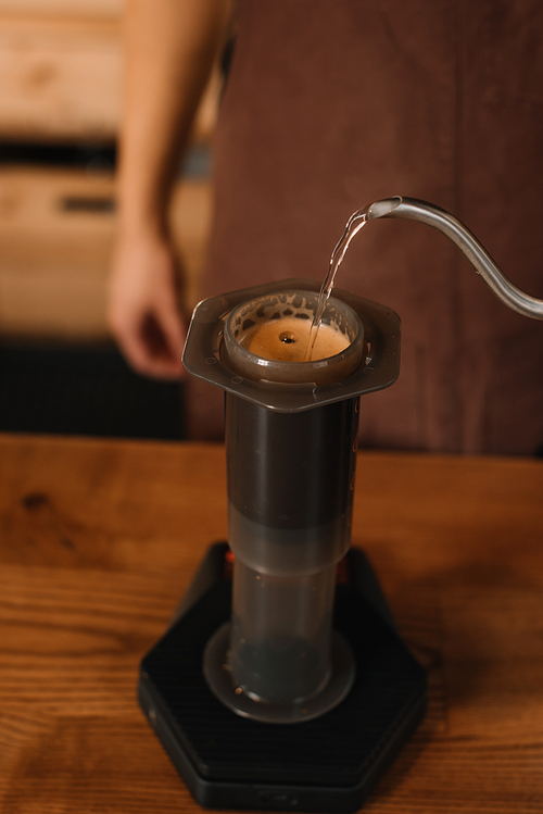 cropped view of barista pouring water from kettle in aeropress while preparing coffee