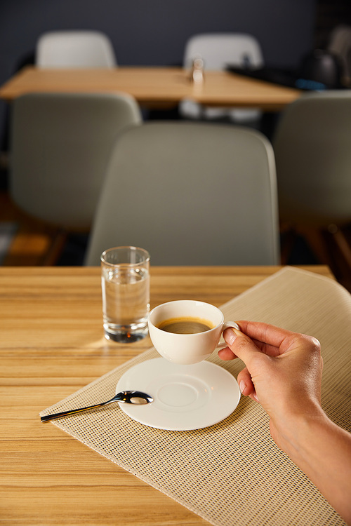 cropped view of woman holding cup with coffee near glass of water in cafe