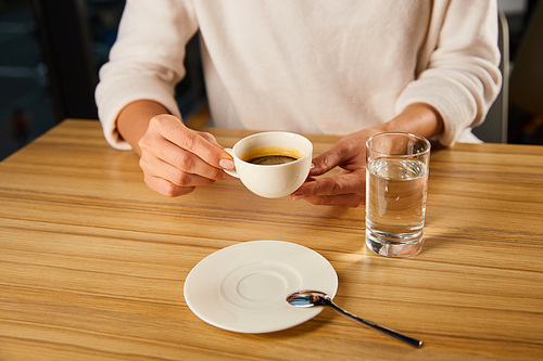 cropped view of woman holding cup of hot coffee near glass of fresh  water in cafe