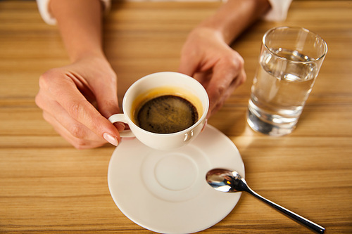 selective focus of woman holding cup of coffee near glass of water in cafe